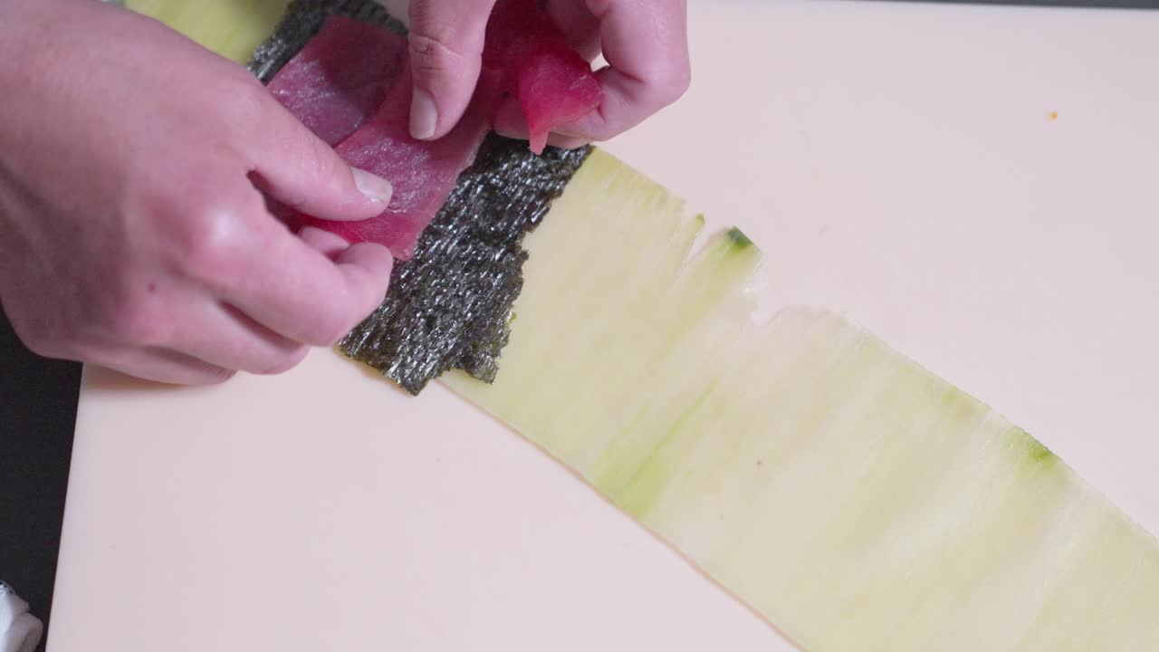 Overhead shot of fresh tuna slices being carefully placed on cucumber for sushi. Perfect for showcasing sushi preparation, Japanese cuisine, and culinary techniques in food presentations.