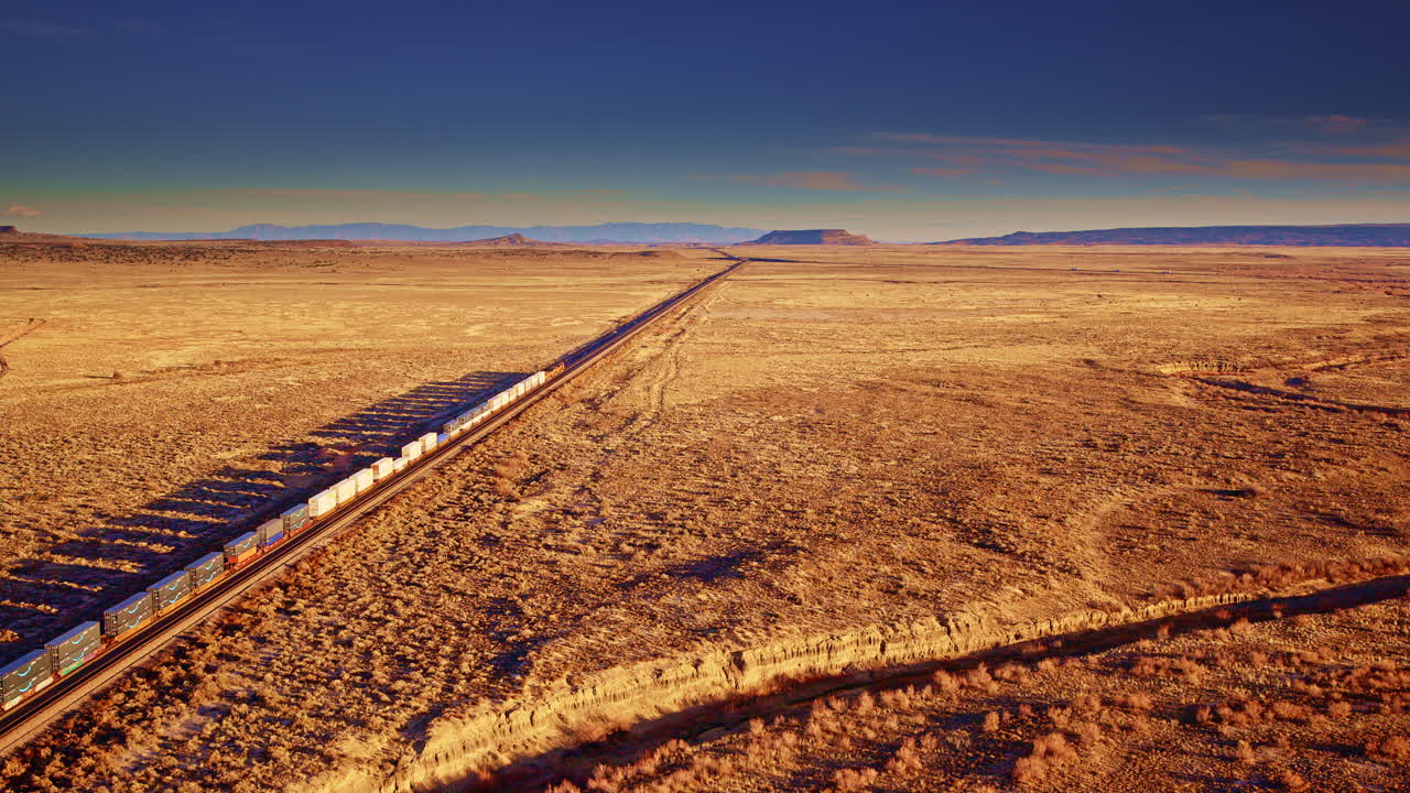 Ampia ripresa con drone di un treno merci che attraversa montagne e pianure occidentali, trasporto ferroviario, rete logistica