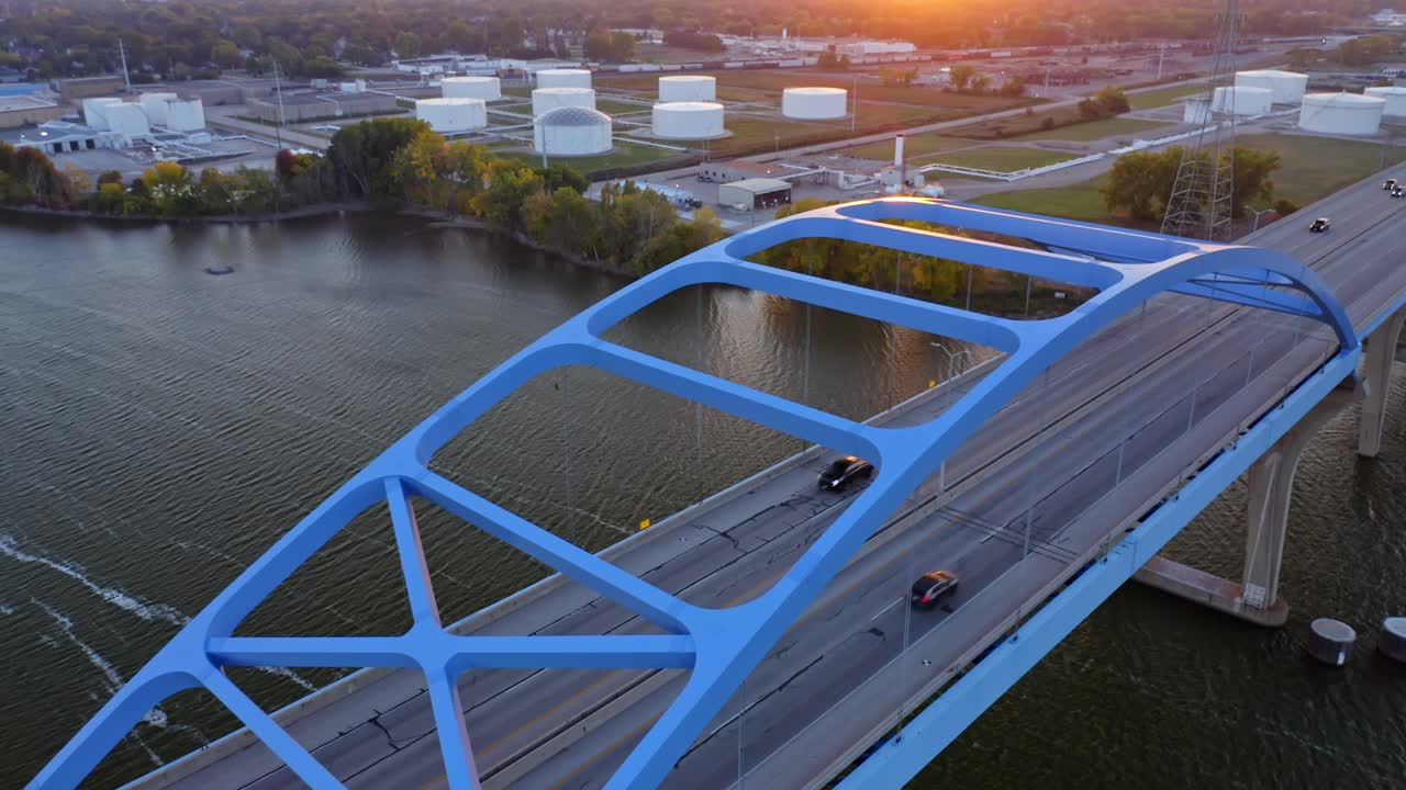 Drone captures an overhead view of a blue truss bridge carrying traffic over a river, highlighting precision engineering, rhythmic geometry, and contrasting textures of steel and water