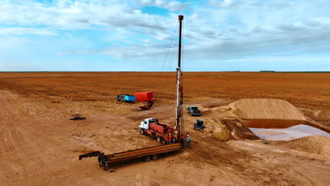 derrick lifting a metal pipe up with the help of a hook. men arrange the equipment for drilling oil or gas. agricultural wheat fields at backdrop.