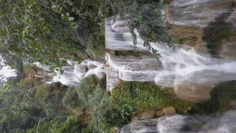 aerial retreats from mountain jungle waterfall through trees in laos