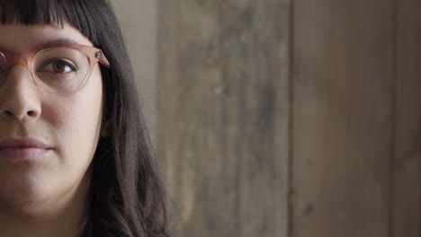 portrait-of-young-hipster-woman-looking-serious-at-camera-wearing-stylish-glasses-on-wooden-background