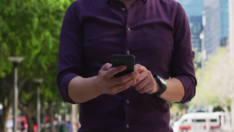 Mid-section-of-man-using-smartphone-while-standing-on-the-street