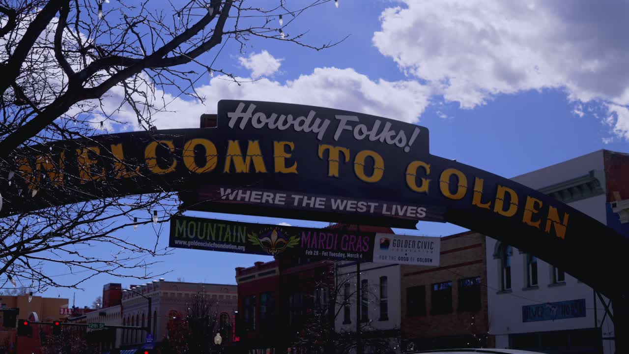 Welcome sign downtown Golden Colorado winter clouds shade blue sky Denver Front Range suburb city Boulder Lookout Mountain Table Mountain Clear Creek tree business slide left motion