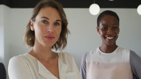 portrait of two diverse female colleagues standing and smiling in office