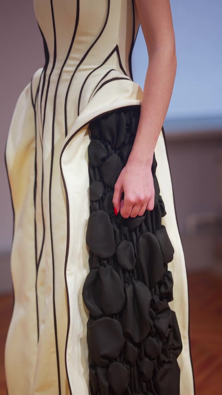 Primo piano di un capo d'alta moda con elementi in tessuto scultorei neri attaccati a una base strutturata, combinati con materiale bianco liscio e sottili linee nere.