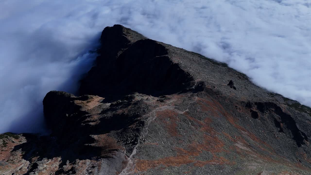 Aerial view of a rugged rocky ridge in the High Tatras, partially surrounded by dense clouds. The sharp crest and barren terrain highlight the dramatic alpine landscape