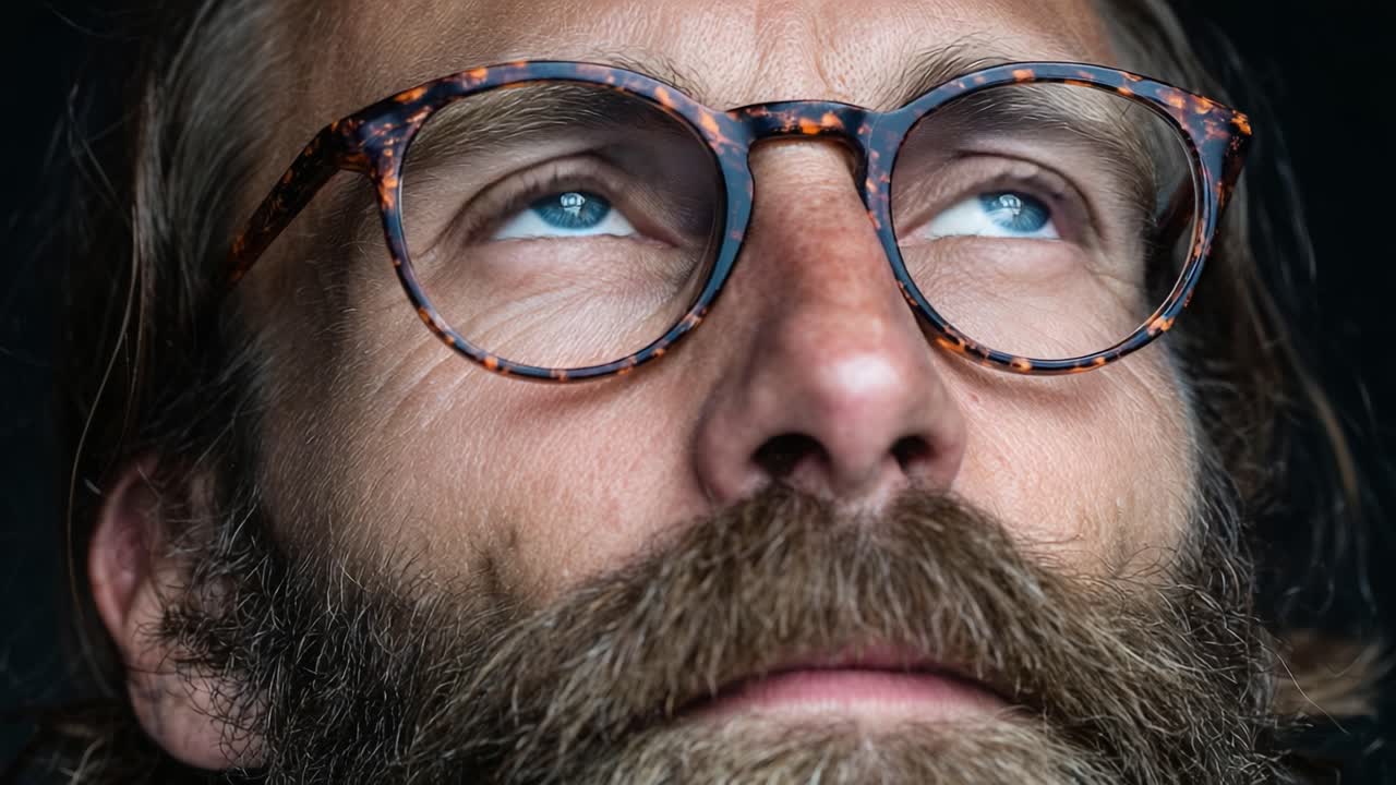 A Close-Up Portrait of a Thoughtful Individual with Distinctive Glasses and a Thick Beard, Capturing Intensity and Depth in Their Expression