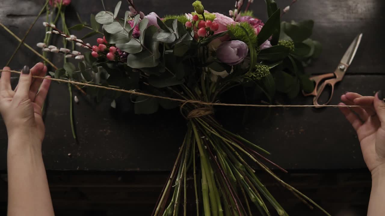 un hermoso ramo de flores decorado por un florista se encuentra en una mesa. la niña lo aprieta firmemente con una cuerda en los tallos. vista desde arriba