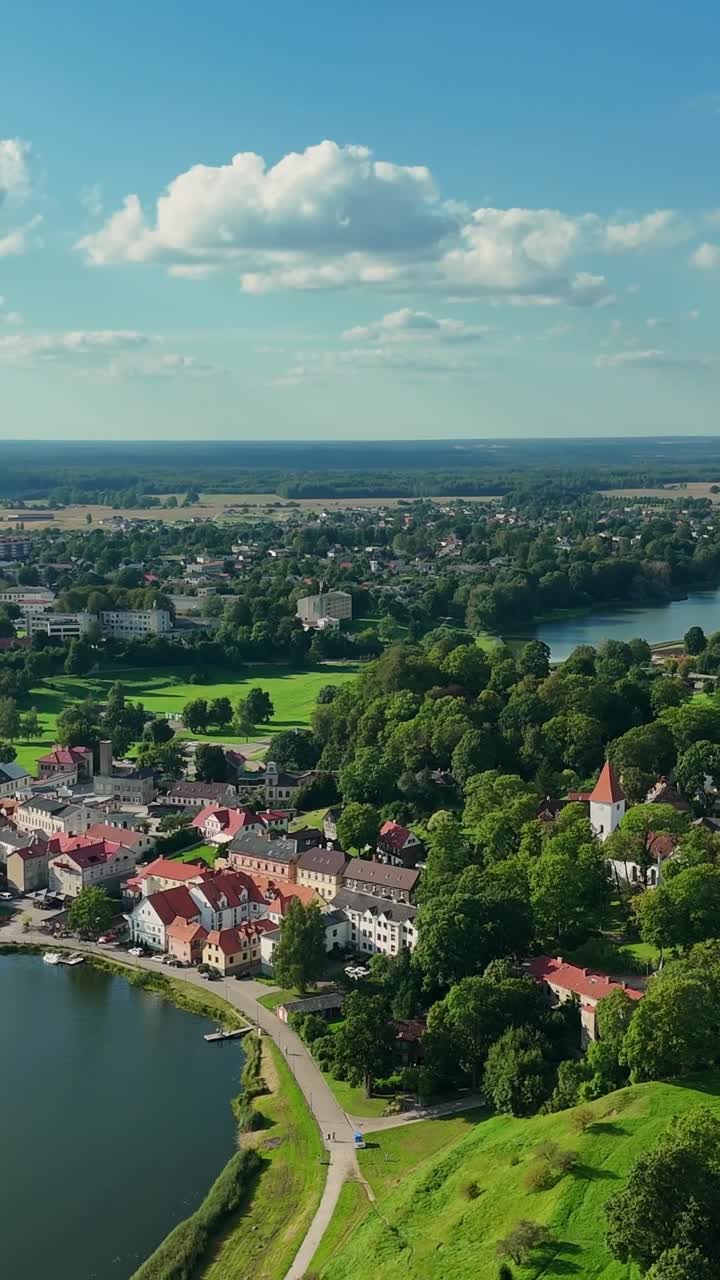 Vertical pan aerial shot of Talsi, Latvia, showing lakes, red-roofed houses, and lush green hills