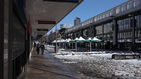 people walking along a snowy and sunny pedestrianised shopping street in a city centre