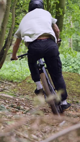 Vertikales-Video-Eines-Mannes-Auf-Dem-Mountainbike,-Der-In-Der-Luft-Auf-Einem-Feldweg-Durch-Den-Wald-Springt