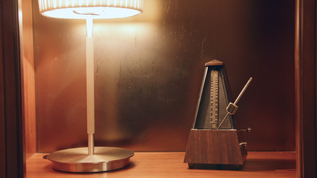 Static shot of a shelf that a metronome is sitting on and a hand comes in and sets the pendulum swinging