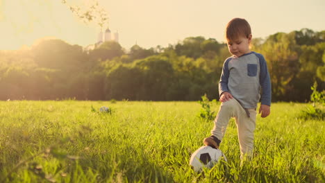 Niño-Parado-En-El-Césped-Con-Una-Pelota-De-Fútbol-Al-Atardecer.