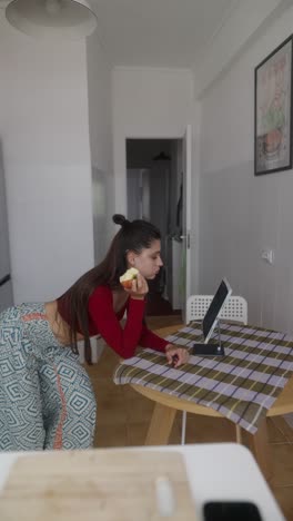 woman eating apple and using tablet in kitchen