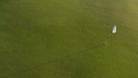 pasando por encima y más allá de una bandera blanca en un campo de golf verde