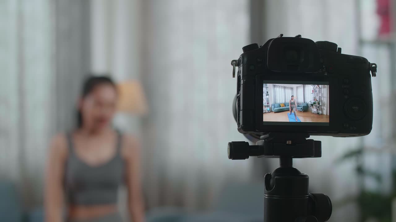 in der nähe eines kameramonitors, die eine asiatische trainerin in sportkleidung aufzeichnet, die yoga in hoher lunge-pose macht, während sie zu hause übungen unterrichtet