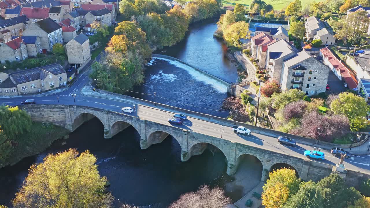 Aerial drone frames Wetherby Bridge, Grade II listed monument spanning River Wharfe, with town-centre roads, autumn foliage, classic stone houses and riverside flats