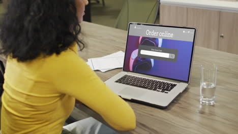 mujer biracial en la mesa usando portátil, compras en línea para gamepads, cámara lenta