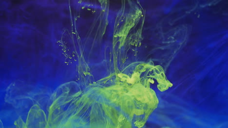 video en cámara lenta de tinta de acuarela amarilla mezclándose en agua contra un fondo azul