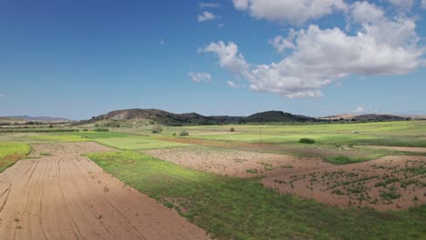 drone ascends above sprawling agricultural landscape with sandy plots and grassy fields