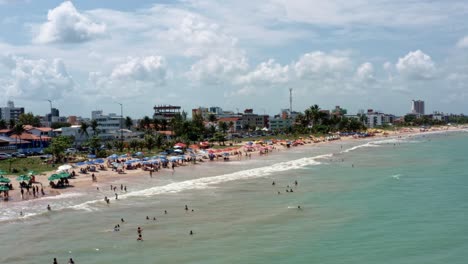 Dolly-out-aerial-shot-of-intermares-beach-in-Cabedelo,-Brazil-with-Brazilians-and-tourists-enjoying-the-ocean-near-the-costal-capital-of-Joao-Pessoa-in-the-state-of-Paraiba-on-a-warm-sunny-summer-day