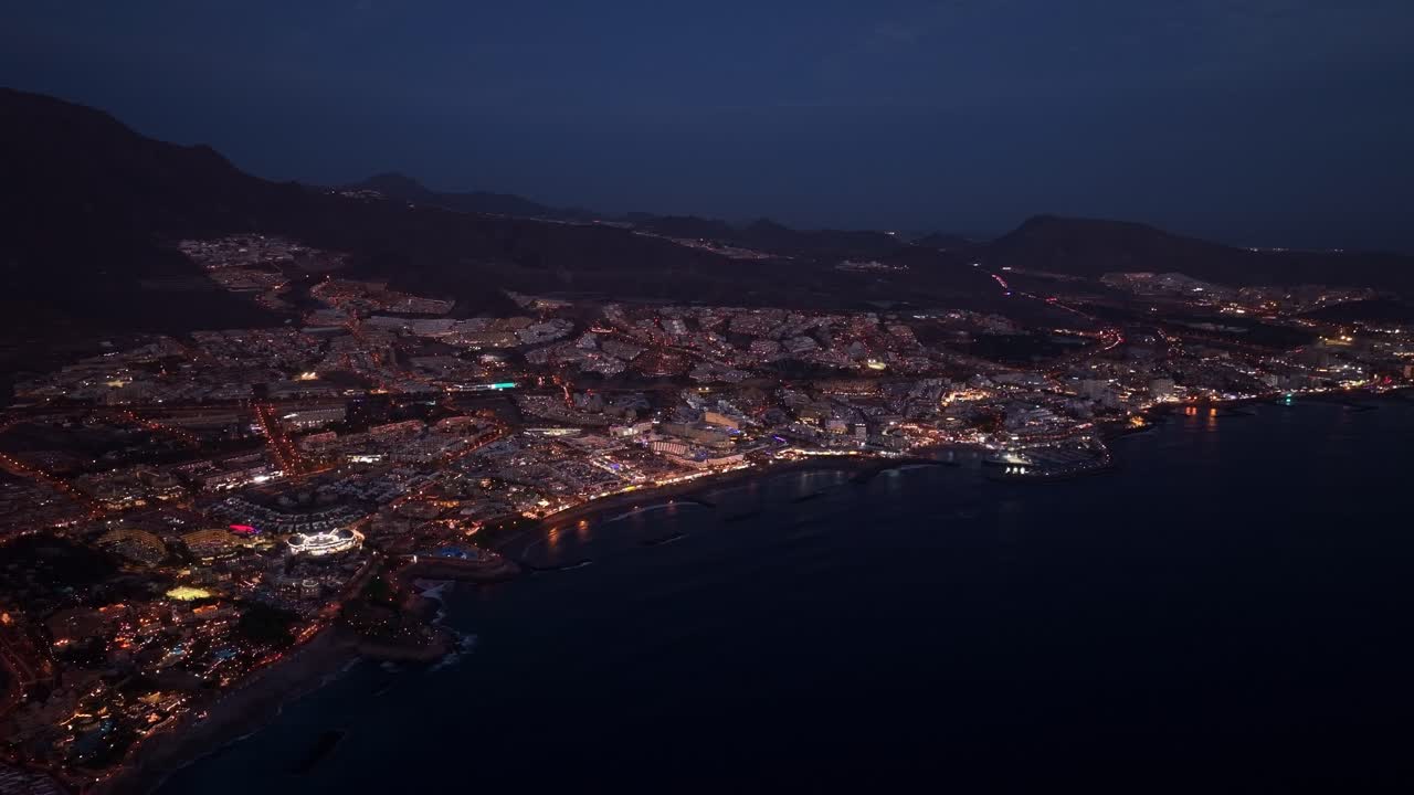 Costa Adeje sulla costa sud-occidentale di Tenerife, illuminata di notte, veduta aerea panoramica, una fila di traffico si dirige verso la città dalle colline in lontananza