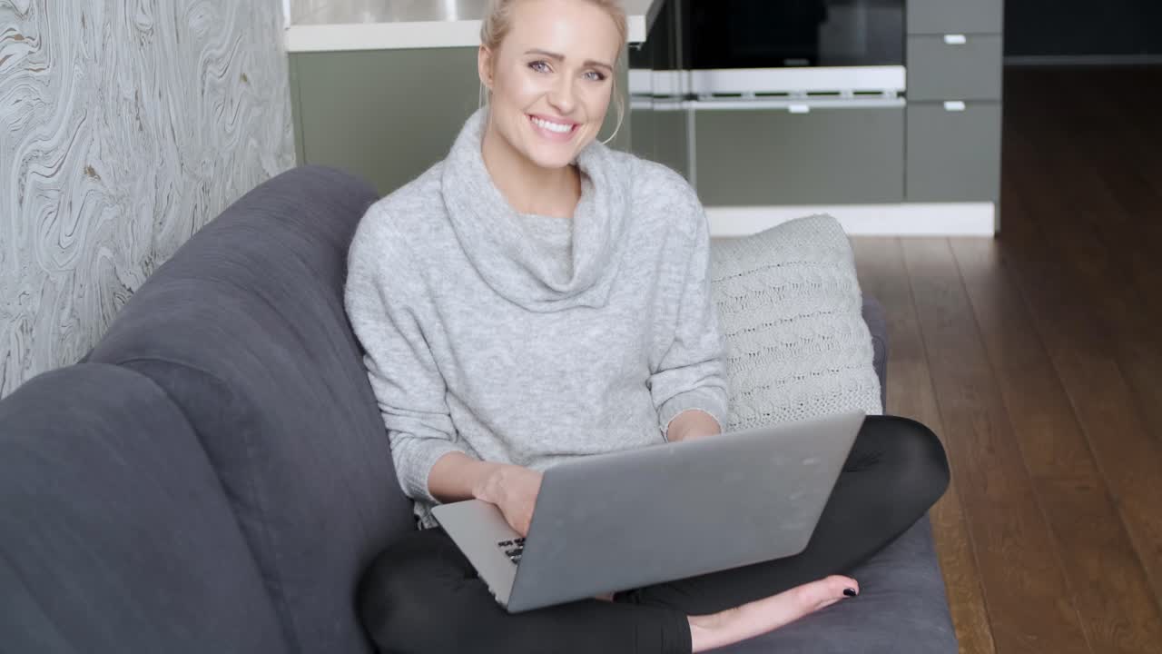 Middle aged woman sitting on sofa in her living room and working on laptop