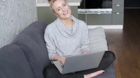Middle-aged-woman-sitting-on-sofa-in-her-living-room-and-working-on-laptop