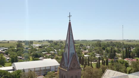 cierre orbital de una torre de iglesia de estilo romántico y cruce con la ciudad de santa anita y la campiña de entre ríos en el fondo, argentina