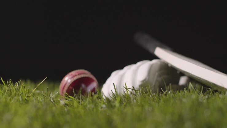 Natura morta di cricket con primo piano di mazza, palla e guanti adagiati sull'erba, messi a fuoco