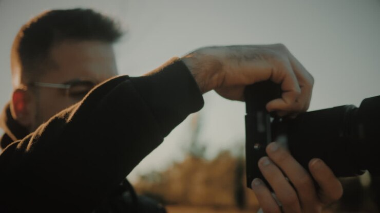 Focused young male landscape photographer lifts a DSLR or mirrorless camera and takes a photo of nature at sunset