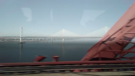 forth road bridge and queensferry crossing from inside a moving train on the forth railway bridge