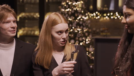 close up view of a red haired girl wearing elegant clothes while talking with her friends and holding a glass of champagne at the new year's party 1