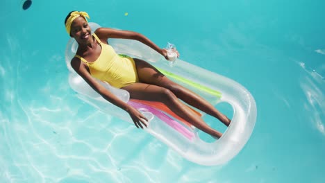 atractiva mujer afroamericana acostada en una bebida inflable y sonriendo en la piscina