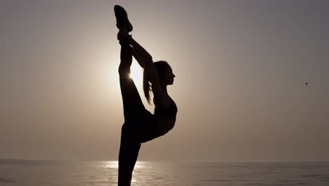 woman black silhouette on sunrise sky background. young active girl standing, doing vertical twine, stretching to keep fit. gourgeous sea view