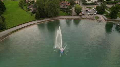 large fountain with a red light inside pouring out water from it into the lake below peaceful atmosphere of hidden city under mountains different coloured houses footpath by the shore and little boat