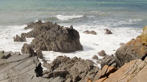 tomada amplia de las olas que chocan contra rocas sedimentarias dentadas en el mar de cornualles en el muelle de hartland, stoke, hartland, bideford