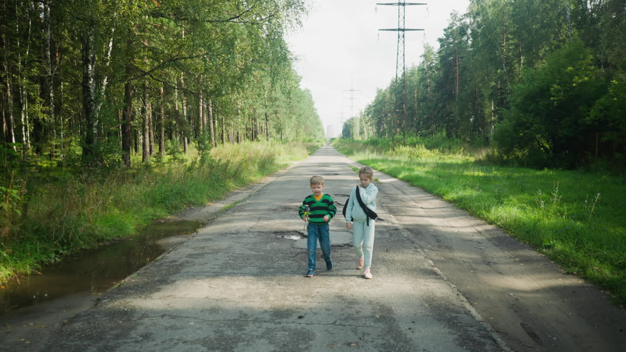 Young school friends walk side by side along paved road through peaceful forest area, surrounded by tall trees and green grass, enjoying serene moment on quiet path under daylight