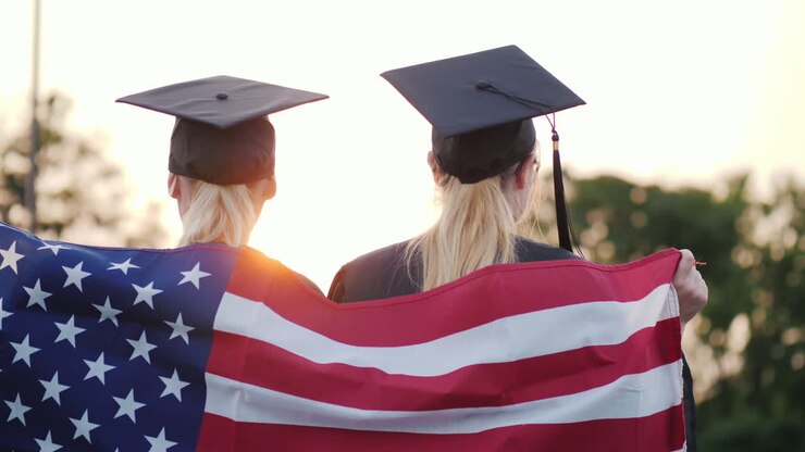 To universitetskandidater i kjortel og studenterhue med det amerikanske flag