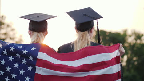 Zwei-College-Absolventen-In-Kleidern-Und-Mützen-Mit-Der-Amerikanischen-Flagge