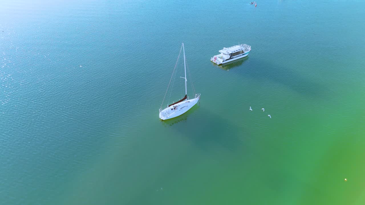 Aerial footage of boats gently floating in Akaroa Harbour, New Zealand, under clear skies with vibrant turquoise waters