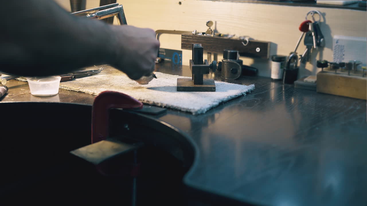 jeweler melts metal in crucible with gas burner at table