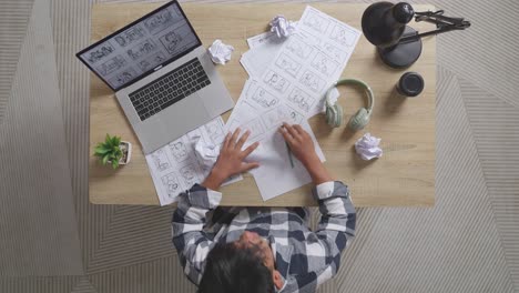 top view of unsatisfied asian male artist crumples paper while drawing storyboard for the film on the table with a laptop and headphones in the studio