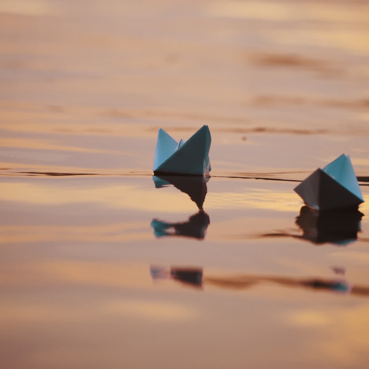 Two blue paper ships on water outdoors. Origami boats floating on the water surface in the evening. Close-up.