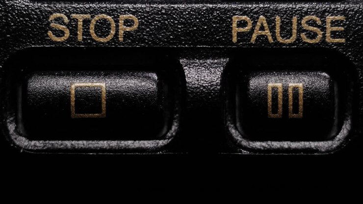 Finger pressing black Stop and Pause buttons with gold lettering on a vintage media player