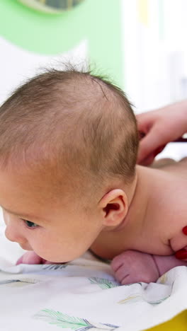 adorable baby lying naked on its belly and holding head up. pediatrician puts stethoscope to kid's back. close up. vertical video