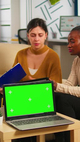 vertical video diverse women sitting at table discussing strategy with green screen laptop