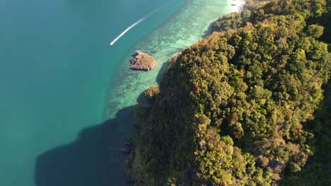 aerial-top-down-view-of-limestone-mountains-at-Ko-Poda-Island-surrounded-by-turquoise-blue-ocean-as-a-thai-longtail-boat-passes-by-on-a-sunny-morning-in-Krabi-Thailand