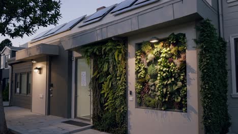 modern, eco conscious house stands illuminated at dusk, featuring a lush vertical garden and solar panels on the roof, highlighting sustainable and green building practices